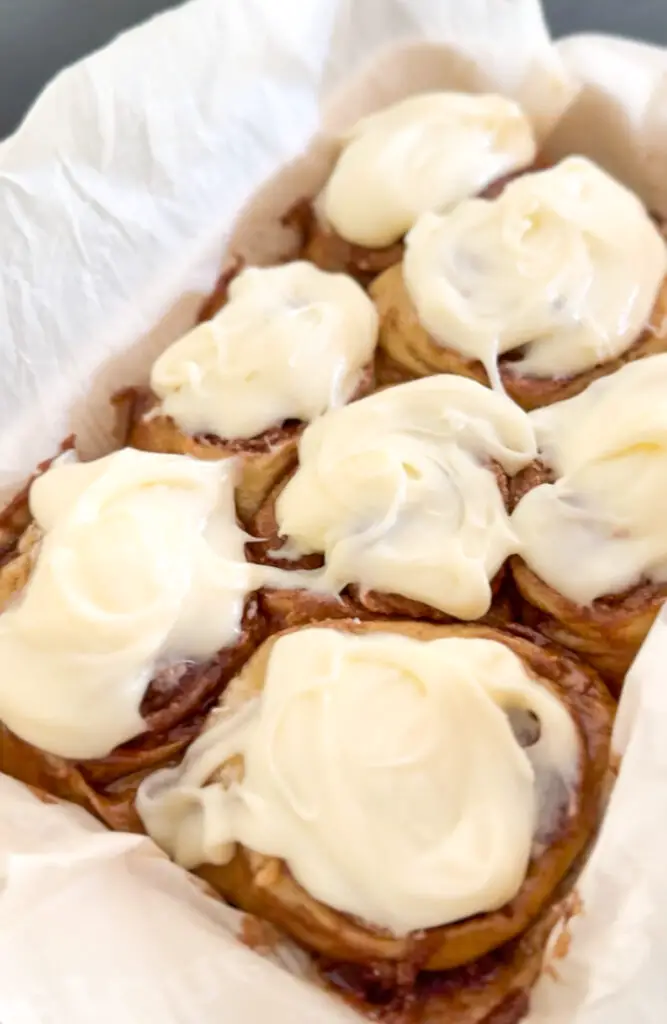 cinnmon rolls with cream cheese topping. in dish with parchment paper.